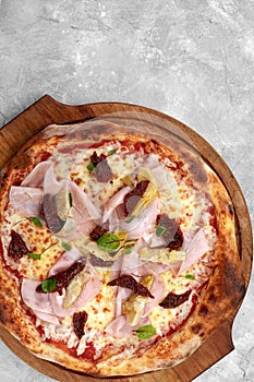 pizza with veal, ham, cheese and sun-dried tomatoes on a gray table