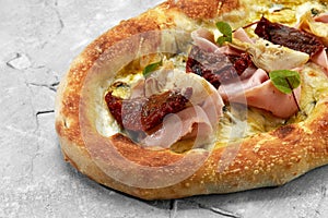 pizza with veal, ham, cheese and sun-dried tomatoes on a gray table