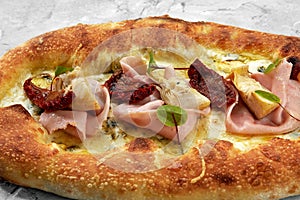 pizza with veal, ham, cheese and sun-dried tomatoes on a gray table