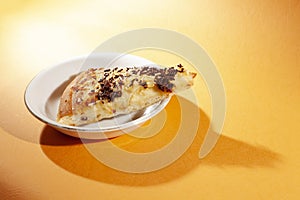 Pizza on white ceramic plate, with cheese and chocolate sprinkles, on orange lighting background