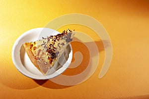 Pizza on white ceramic plate, with cheese and chocolate sprinkles, on orange lighting background