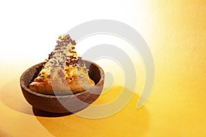 Pizza on wooden plate, with cheese and chocolate sprinkles, on orange background