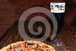 Pizza on wooden table near a glass of dark beer