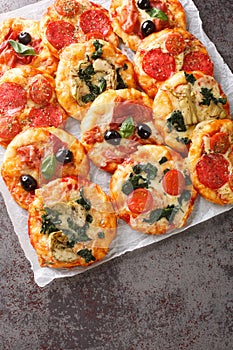 Pizzette small pizzas with various toppings close-up on parchment. Vertical top view photo