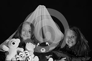 PJs party for children. Girls with happy faces playing with teddies under blanket