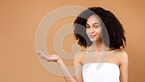 Place for ad. Beautiful latin lady advertising new beauty product on her empty palm, brown background, free space