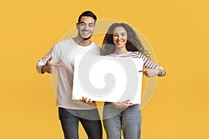 Place For Ad. Happy Arab Couple Holding And Pointing At Blank Placard