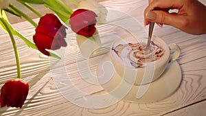 Place a Cup of coffee with a latte pattern on a white wooden table with a bouquet of tulips. Stirring coffee in a Cup.