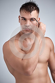 A place for every hair. Portrait of a young handsome man tweezing his eyebrows against a grey background.