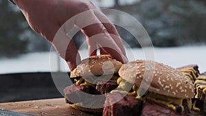 Place loaf on top of juicy pastrami steak. Assembling delicious burger with meat, mustard, gherkins on the street in