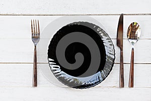 Place setting table food with set of black plate on the table dinner / empty plate spoon fork and knife on wood table , top view