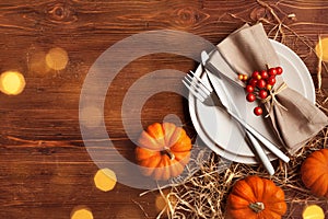 Place setting for Thanksgiving dinner with plate, napkin, cutlery and pumpkins on wooden table top view