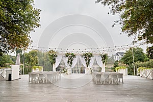 Place for wedding ceremony with wedding arch decorated with palm leaves, orchid flowers and floral peacocks and white chairs