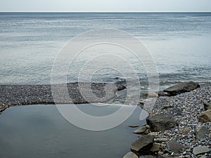 The place where a small river flows into the sea. Winter on the Black Sea. Empty coast. Beach of boulders and small pebbles