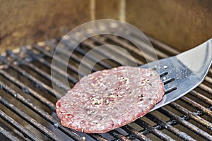 Placing a seasoned hamburger on a hot grill