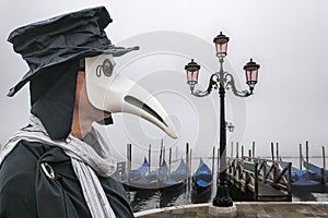 Plague doctor against gondolas during foggy day in Venice, Italy, Epidemic symbol photo