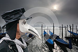 Plague doctor against gondolas during foggy day in Venice, Italy, Epidemic symbol