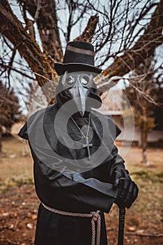 Plague doctor with a cane and a classic dark garb with a cross photo