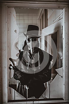 A plague doctor with a cane and a classic dark garb with a cross photo