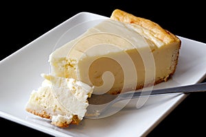 Plain baked cheesecake with cake on fork on white ceramic plate.