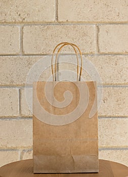 Plain blank brown paper bag in front of a beige brick background