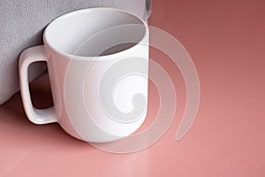 Plain blank white 11oz cup in front of a grey cushion on a pink shiny surface
