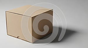 A plain, brown cardboard box sits on a smooth, light gray surface. The box is cubic