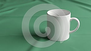 A plain white ceramic mug stands on a smooth green fabric background