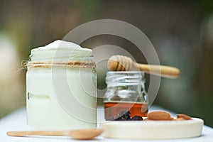 Plain yoghurt in white bowl, honey, cereal, raisin and wood spoon on white wooden table background