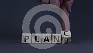 Plan B or C symbol. Businessman turns a wooden cube and changes words Plan B to Plan C. Beautiful grey table, grey background,