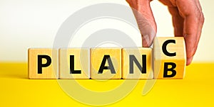 Plan B or C symbol. Businessman turns a wooden cube and changes words Plan B to Plan C. Beautiful yellow table, white background,