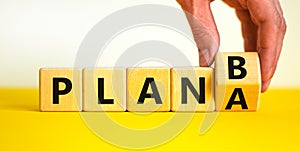 Plan A or B symbol. Businessman turns a wooden cube and changes words Plan A to Plan B. Beautiful yellow table, white background,