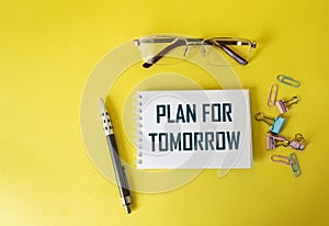 PLAN FOR TOMORROW, text in a notebook  near glasses, a pen and paper clips