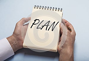 Plan word on notebook in male hands over blue table
