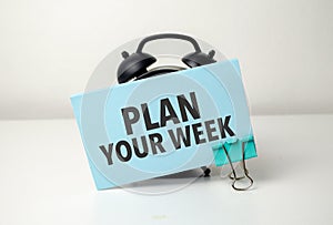 PLAN YOUR WEEK is written in a blue sticker near a black alarm clock