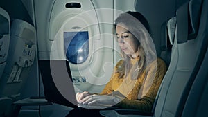Plane cabin at night with a woman operating a laptop