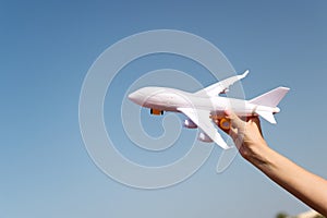 Plane in female hand clear blue sky background copy space. Travel and vacation. Book tickets now. Toy white plane fly