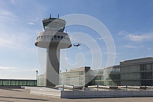 A plane flies next to the control tower at Barcelona Airport, Sp