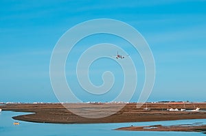 The plane flies to the airport over the river in the city of Faro in Portugal. Many boats on a sunny day by the river .
