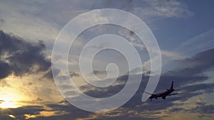 Plane flies toward sunset. Sun`s rays make their way through the purple clouds