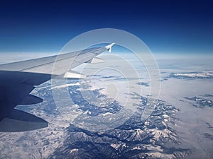 Plane flight above the Carpathian Mountains snowy peaks. Blue skyline and airplane wing seen through the window