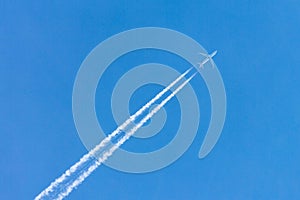 Plane flying high in clear blue sky leaving long white trail