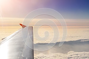 Plane flying over clouds at dawn. Airplane wing over beautiful cloudscape during dramatic colorful sunset or sunrise. Travel and