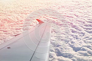 Plane flying over clouds at dawn. Airplane wing over beautiful cloudscape during dramatic colorful sunset or sunrise. Travel and