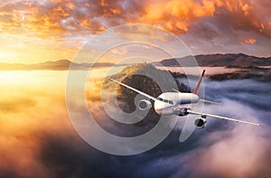 Plane is flying over mountains in low clouds at golden sunrise