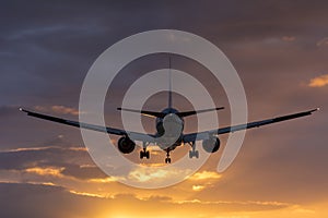 Plane flying towards the runway during a cloudy sunrise.