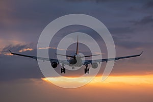 Plane flying towards the runway during a cloudy sunrise.