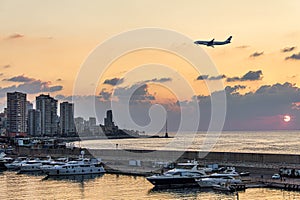 A plane landing over Beirut waterfront skyline during sunset