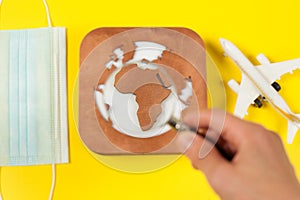 Plane model, face mask, loupe in hand and earth model on a yellow background. Flight impact of coronavirus COVID-19 concept.