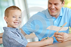 This plane is neat. a father playing with a model airplane while his son smiles widely.